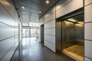 Moderne entreehal aan de Joan Muyskenweg met openstaande lift en glazen schuifdeuren bij de ingang.